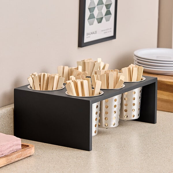 A black Cal-Mil flatware display with wooden sticks in it.
