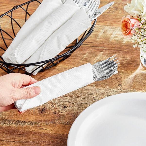 A hand holding a white Choice WrapNap dinner napkin.