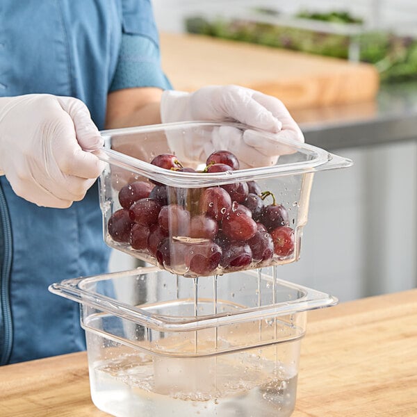 A person in gloves holding a Cambro clear plastic container of grapes.