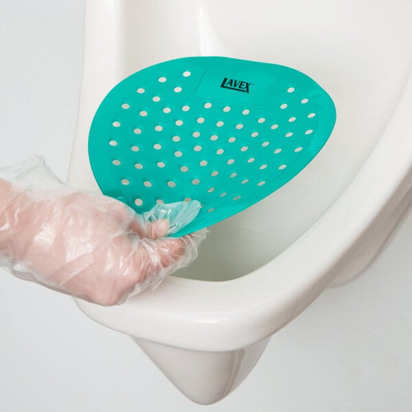 A gloved hand places a green Lavex Mint Scent Deodorized Urinal Screen in a urinal.