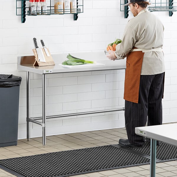 A person wearing an apron standing at a Regency stainless steel work table holding a bowl of vegetables.