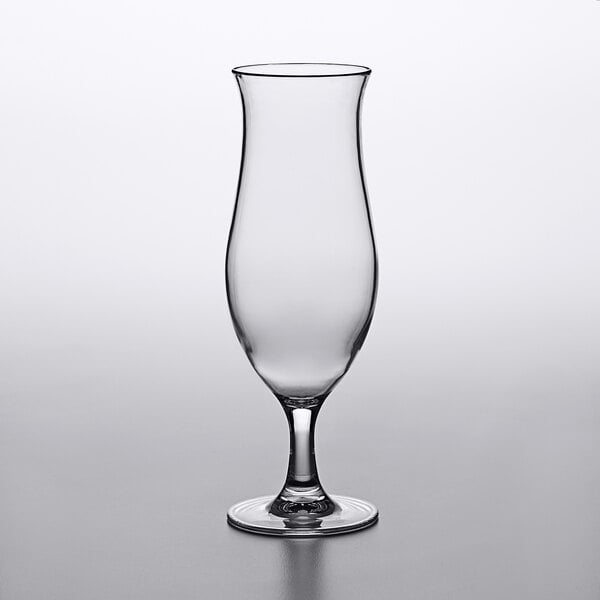 A clear Carlisle plastic hurricane glass with a stem on a table.