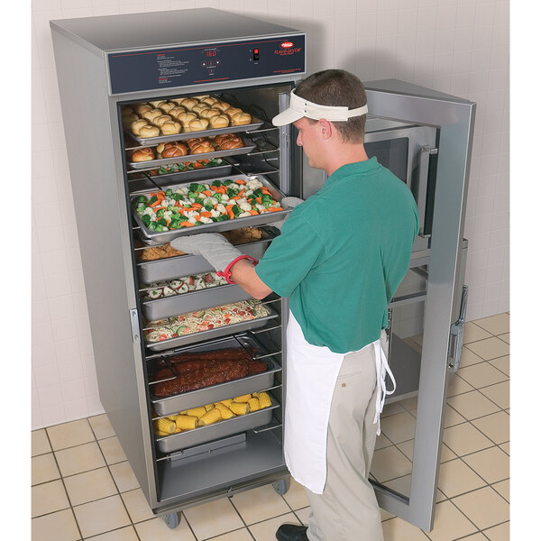 A person putting trays of food into a Hatco Flav-R-Savor holding and proofing cabinet.