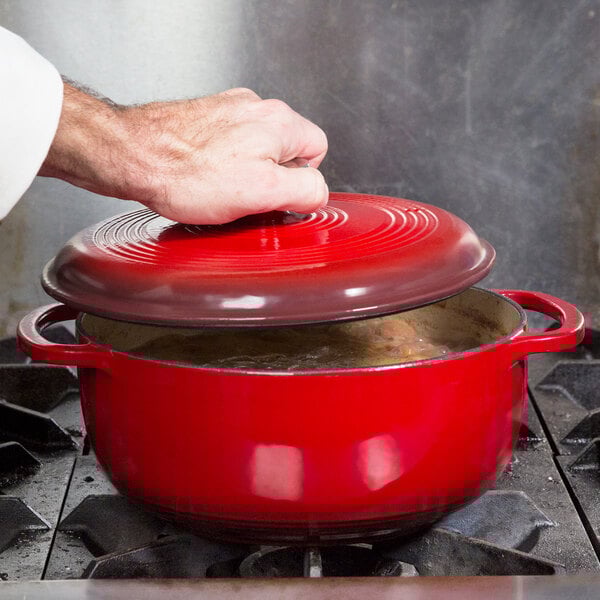 A person putting a lid on a Lodge Island Spice Red Enameled Cast Iron Dutch Oven.