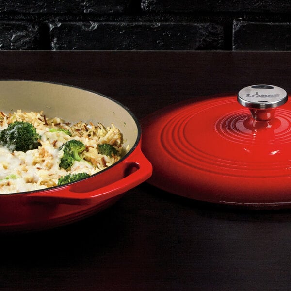 A Lodge Island Spice Red enameled cast iron casserole dish with food in it next to a red lid.