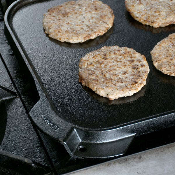 Four hamburger patties cooking on a Lodge cast iron griddle.