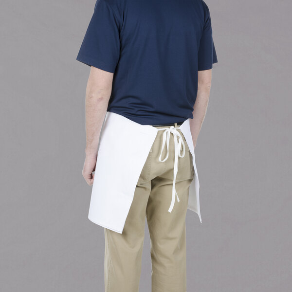 A man wearing a white Chef Revival waist apron on a counter in a professional kitchen.