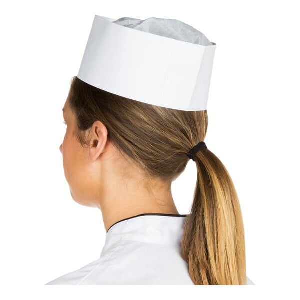 A person with long hair tied in a ponytail is wearing a white paper cap and a white uniform, viewed from behind.