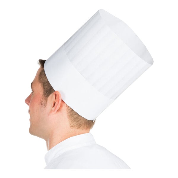 A person is shown in profile wearing a tall, white, pleated chef hat and a white jacket.