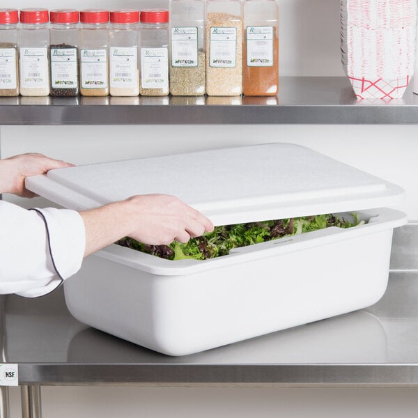 A person opening a Carlisle white container of food with lettuce inside.