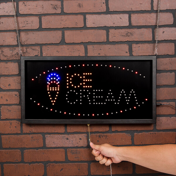 A person's hand holding a black sign that says "Ice Cream" with LED lights.