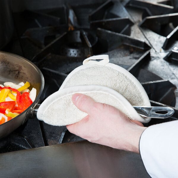 A person using a San Jamar terry cloth pot holder to hold a pan of food.