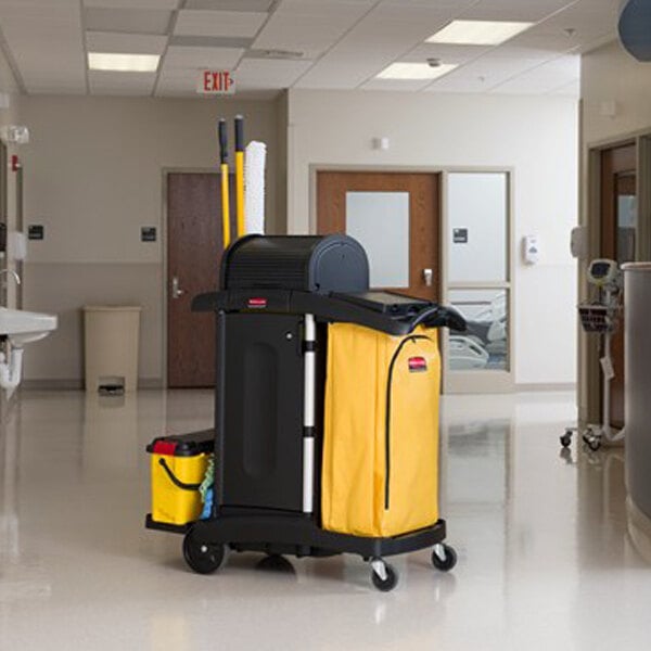 A Rubbermaid janitor cart with a yellow bag and black cabinets.