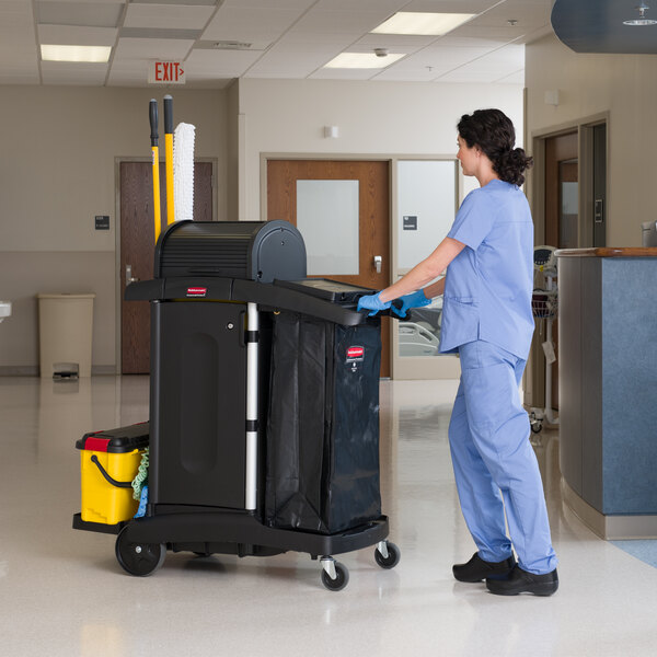 A Rubbermaid Executive High Security Janitor Cart with a locking hood and cabinets being pushed by a person in a hallway.