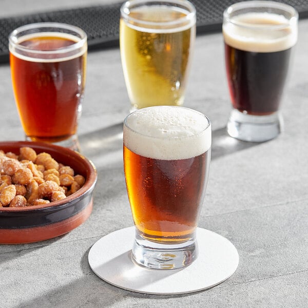 A group of Anchor Hocking Barbary beer tasting glasses filled with beer on a table with a bowl of snacks.