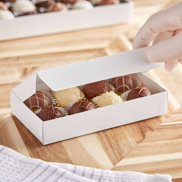 A hand holding a white 1-piece candy box filled with chocolates.