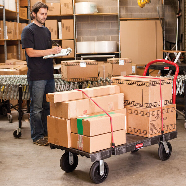 A man standing next to a Rubbermaid platform truck with boxes on it.
