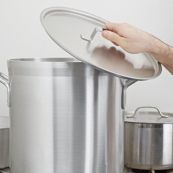 A hand using a Vollrath Torogard aluminum lid to open a large silver pot.