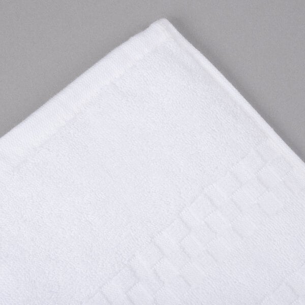 An Oxford Viceroy white terry bath towel with a checkered border and twill hem on a gray surface.