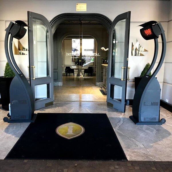 A pair of Bromic Heating BH0510001 Tungsten Smart-Heat portable propane outdoor patio heaters positioned at the entrance of a building.