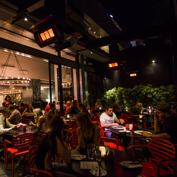 A group of people sitting at tables on a restaurant patio with a Bromic Heating Tungsten Smart-Heat patio heater.