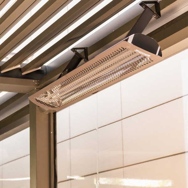 A black electric outdoor patio heater mounted on a wall under a pergola.