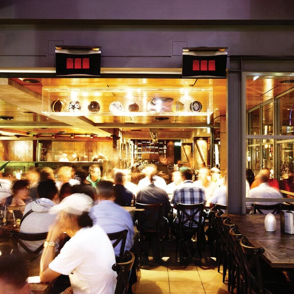 A group of people sitting at tables on a patio with a Bromic Heating Platinum Smart-Heat patio heater.