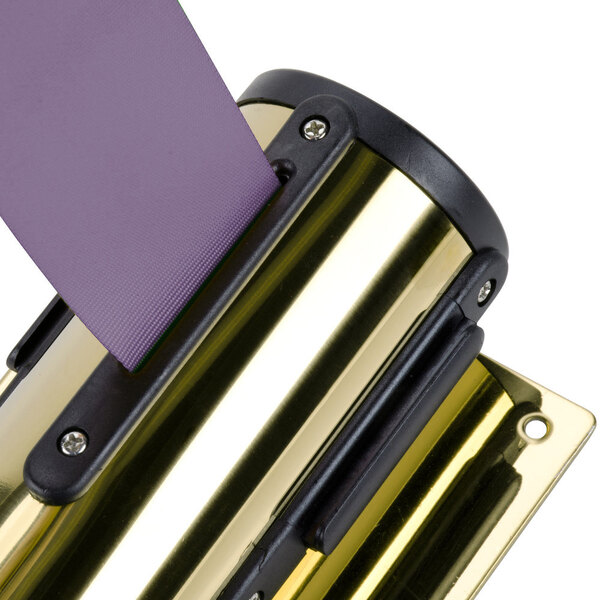 A brass Aarco wall-mount stanchion with a purple retractable belt attached.