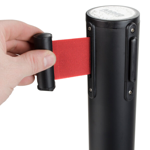 A person holding a red retractable belt on a black Aarco stanchion.