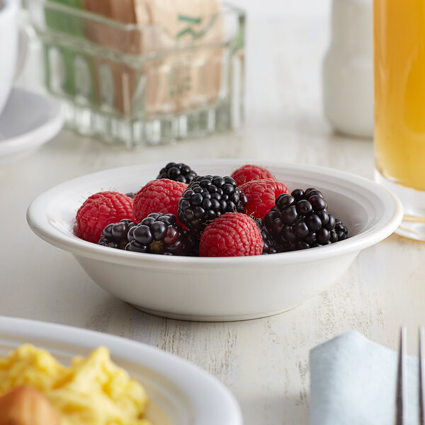 A Tuxton white china monkey dish filled with berries on a table with an omelette and orange juice.