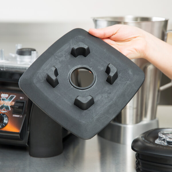 A hand holding a black square Waring jar pad with holes.