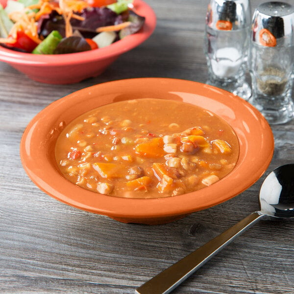 A bowl of soup and a bowl of salad on a table with a spoon.