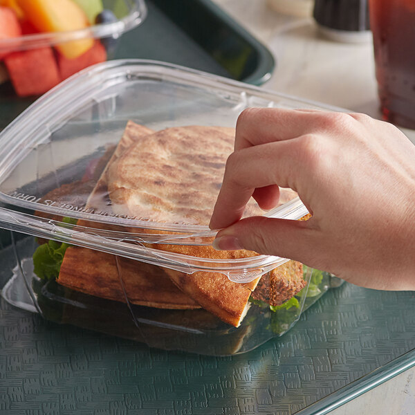 A close up of a hand holding a Dart deli container with food in it.