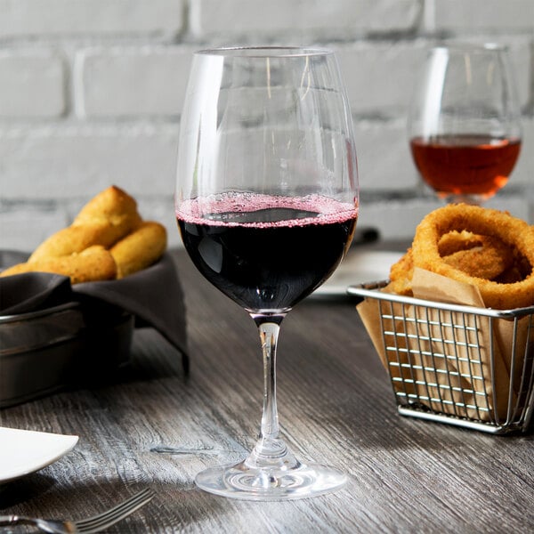 A Thunder Group plastic wine glass filled with red wine on a table with food.