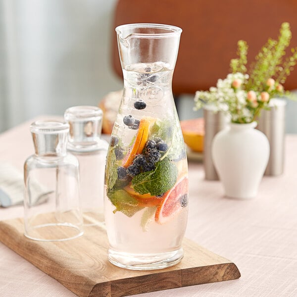 A Libbey glass carafe filled with water and fruit on a wooden board.