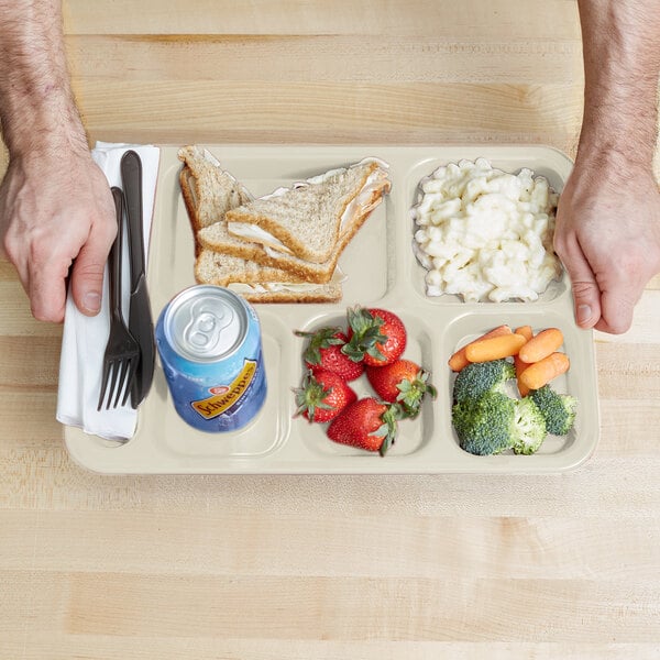 A Carlisle tan 6 compartment tray with a sandwich, fruit, and vegetables.