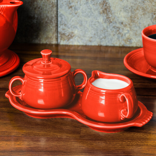 A red Fiesta sugar and creamer tray set on a wooden surface.