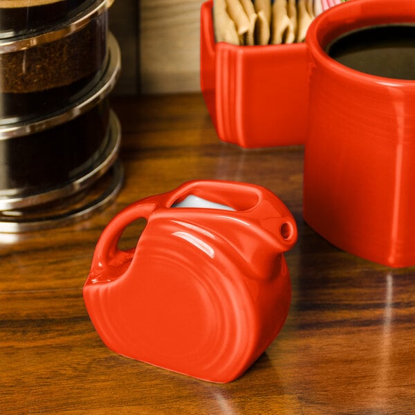 A red disc creamer pitcher on a table.