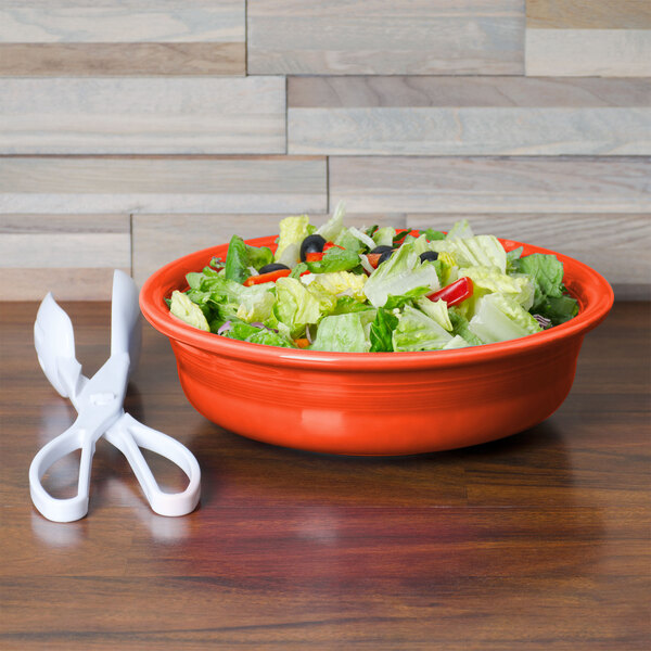 A Fiesta Poppy china bowl filled with salad next to a pair of scissors on a table.