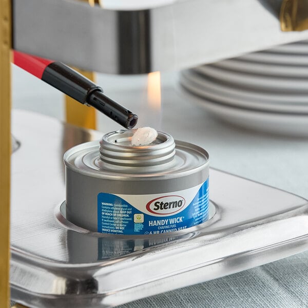 A can of Sterno Handy Wick chafing fuel being lit with a lighter under a food warmer.