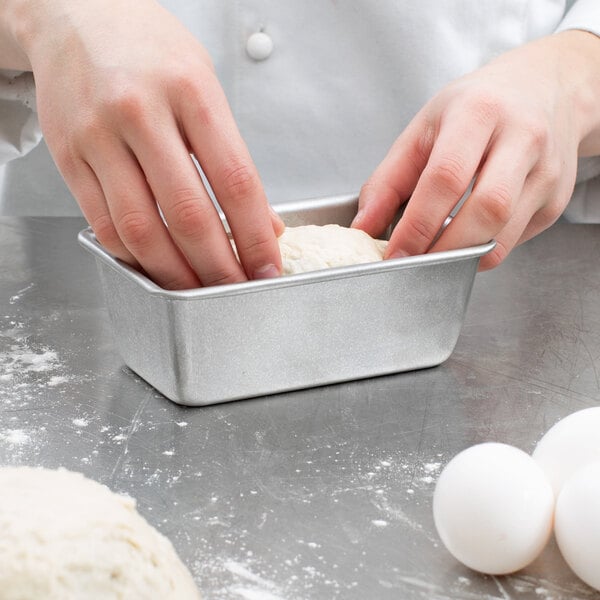 A person's hands kneading dough in a Chicago Metallic aluminized steel bread loaf pan.