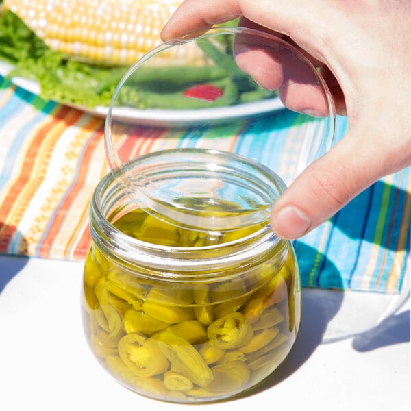 A hand holding a American Metalcraft round PET Mason jar lid over a jar of jalapenos.