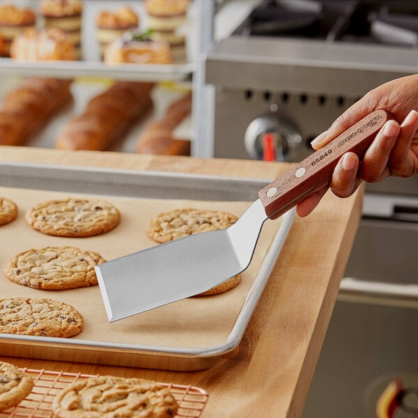 A hand using a Dexter-Russell beveled edge solid turner to lift a cookie from a tray.