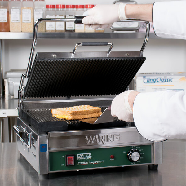 A hand using a Waring Large Handle to cut a sandwich on a grill.