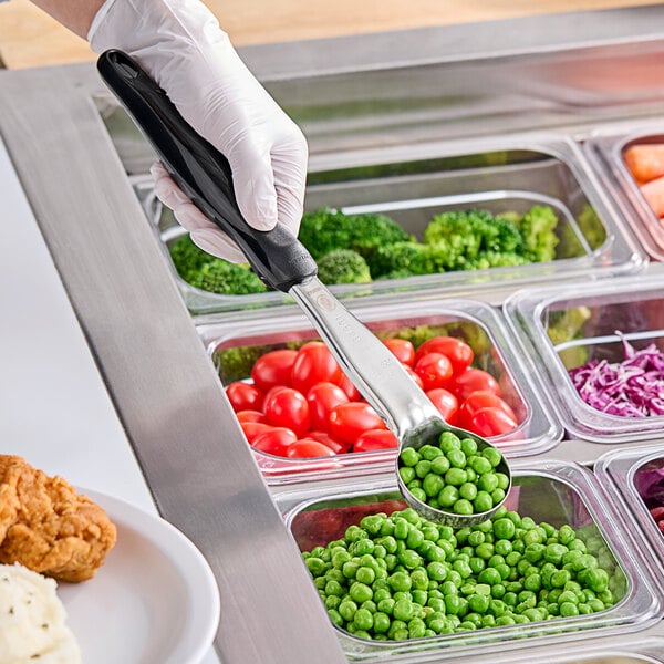 A person holding a Vollrath black solid round spoodle over a container of vegetables.