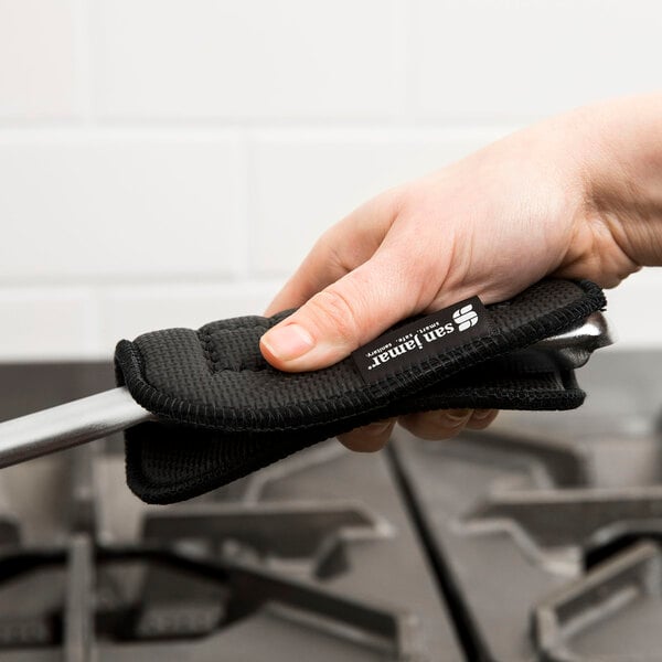 A person using a San Jamar UltiGrips hot pad with a black strap to hold a tool over a stove top.