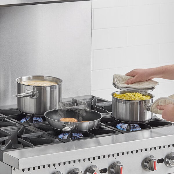 A woman cooking food in a Vollrath Optio stainless steel pot on a stove.