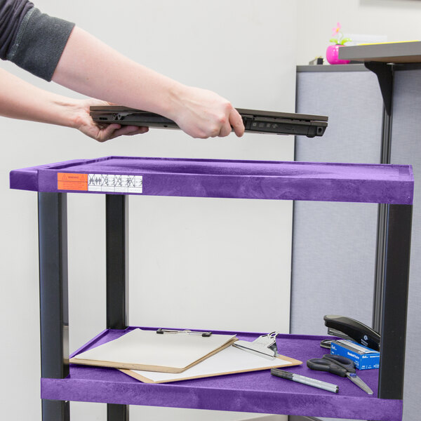 A person holding a laptop on a Luxor purple utility cart.