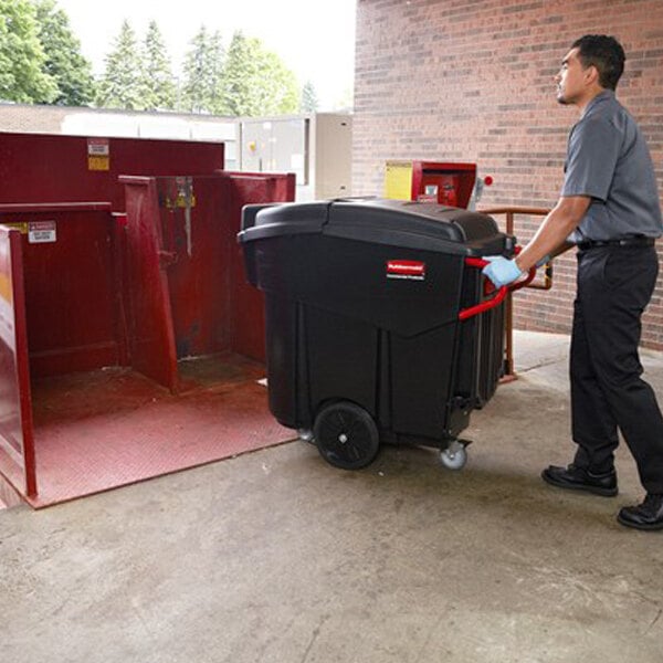 A man pushing a black Rubbermaid Mega Brute waste collector into a building.