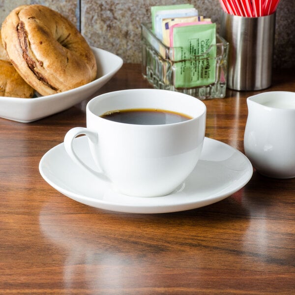 A CAC Majesty bone china saucer with a cup of coffee on a table with a bowl of bagels.